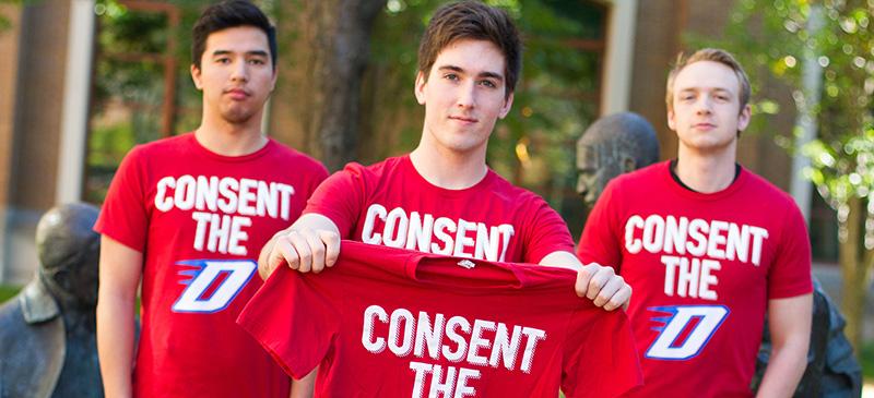 Randy Vollrath (center), a senior at DePaul, holds the preliminary T-shirt design for the Consent the D movement he started.  Vollrath says this is the student response that is “ long overdue” and hopes to put DePaul on the map, demonstrating that students care and are doing something proactive about sexual assault. (Grant Myatt / The DePaulia)