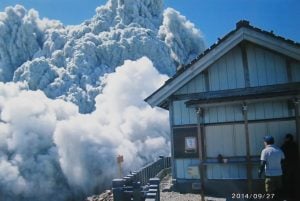 In this Saturday, Sept. 27, 2014 file photo taken by 59-year-old hiker Izumi Noguchi who fell victim to the eruption of Mount Ontake, and was offered to Kyodo News by his wife, Hiromi, Friday, Oct. 3, a hiker standing on the summit shrine compound on Mount Ontake watches dense plumes of gases and ash billowing from the crater as the volcanic mountain starts to erupt. AP Photo/Kyodo News, Izumi Noguchi 
