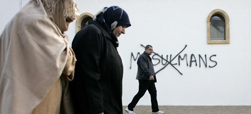 French Muslims walk past anti-Muslim graffiti painted on a Mosque in Saint-Etienne, France. (Laurent Cipriani | AP)