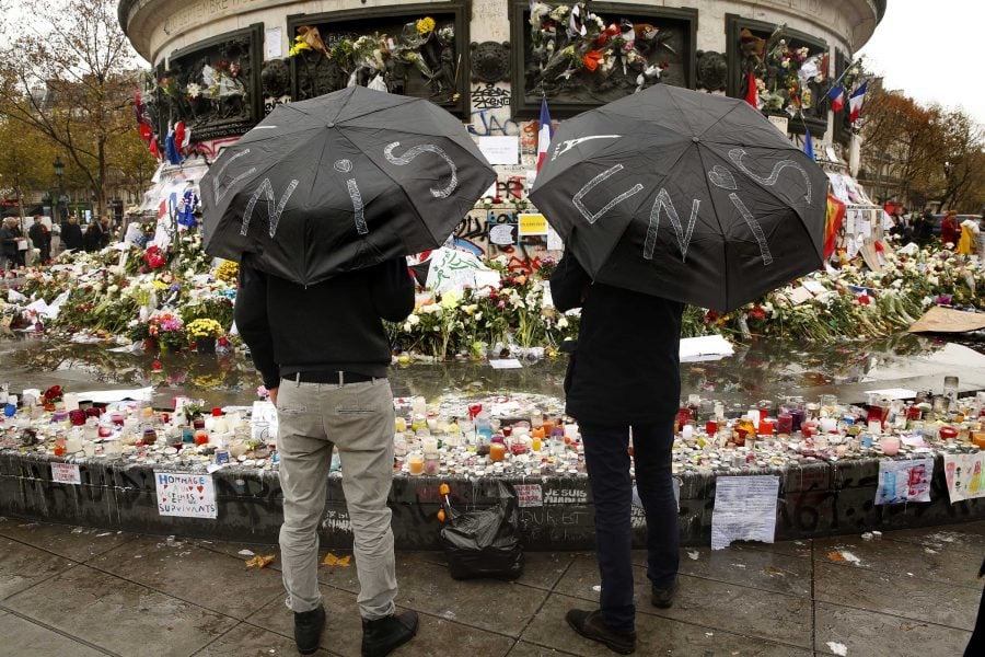 Two men hold umbrellas that say unite while visiting a memorial site in Paris on Thursday, Nov. 19, 2015. (Carolyn Cole/Los Angeles Times/TNS)