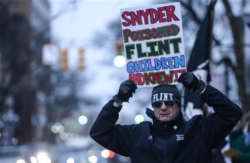 Mike Ahrens of Muskegon, Mich., poses for photo with his sign about Flint's water crisis Monday, Jan. 18, 2016, in Ann Arbor, Mich. Michigan Gov. Rick Snyder responded Monday to criticism from presidential candidate Hillary Clinton during the Democratic debates for his handling of Flint's water emergency, saying Clinton is making it a political issue. (Junfu Han/The Ann Arbor News via AP) LOCAL TELEVISION OUT; LOCAL INTERNET OUT; MANDATORY CREDIT