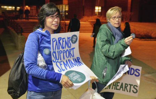 In this Feb. 20, 2017 photo, Iliana Mora and Amanda Nugent hand out signs and buttons in support of an upcoming all-school seminar on civil rights at New Trier High School before a school board meeting at the school's Northfield campus in Northfield, Ill. The school is holding a daylong seminar on civil rights designed to help students in the largely white and affluent school see things from other perspectives on Feb. 28. Conservative groups and some parents have raised concerns about the tone being too liberal. (Brian O'Mahoney/Chicago Tribune via AP)