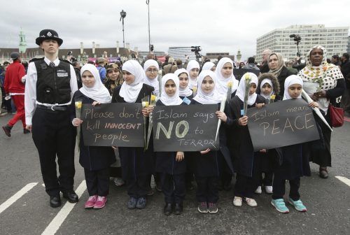 A police officer stands next to muslim girls during a commemorative event to mark last week's attack outside Parliament that killed four people, on Westminster Bridge in London, Wednesday, March 29, 2017. (Yui Mok/PA via AP)