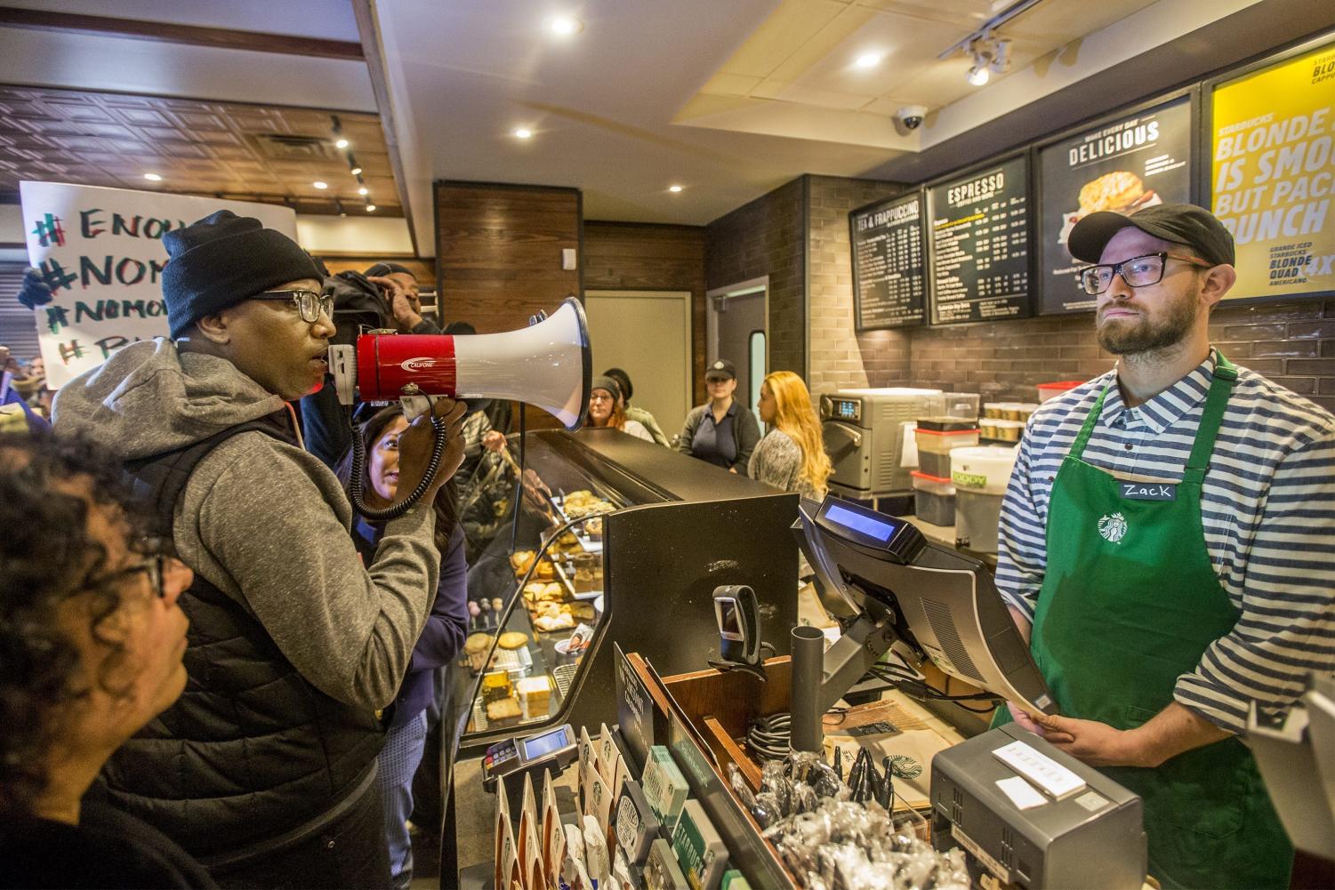 Activist Asa Khalif, left, stands inside a Starbucks, April 15 demanding the firing of the manager who called police resulting the arrest of two black men.
(Michael Bryant | The Philadelphia Inquirer via AP)