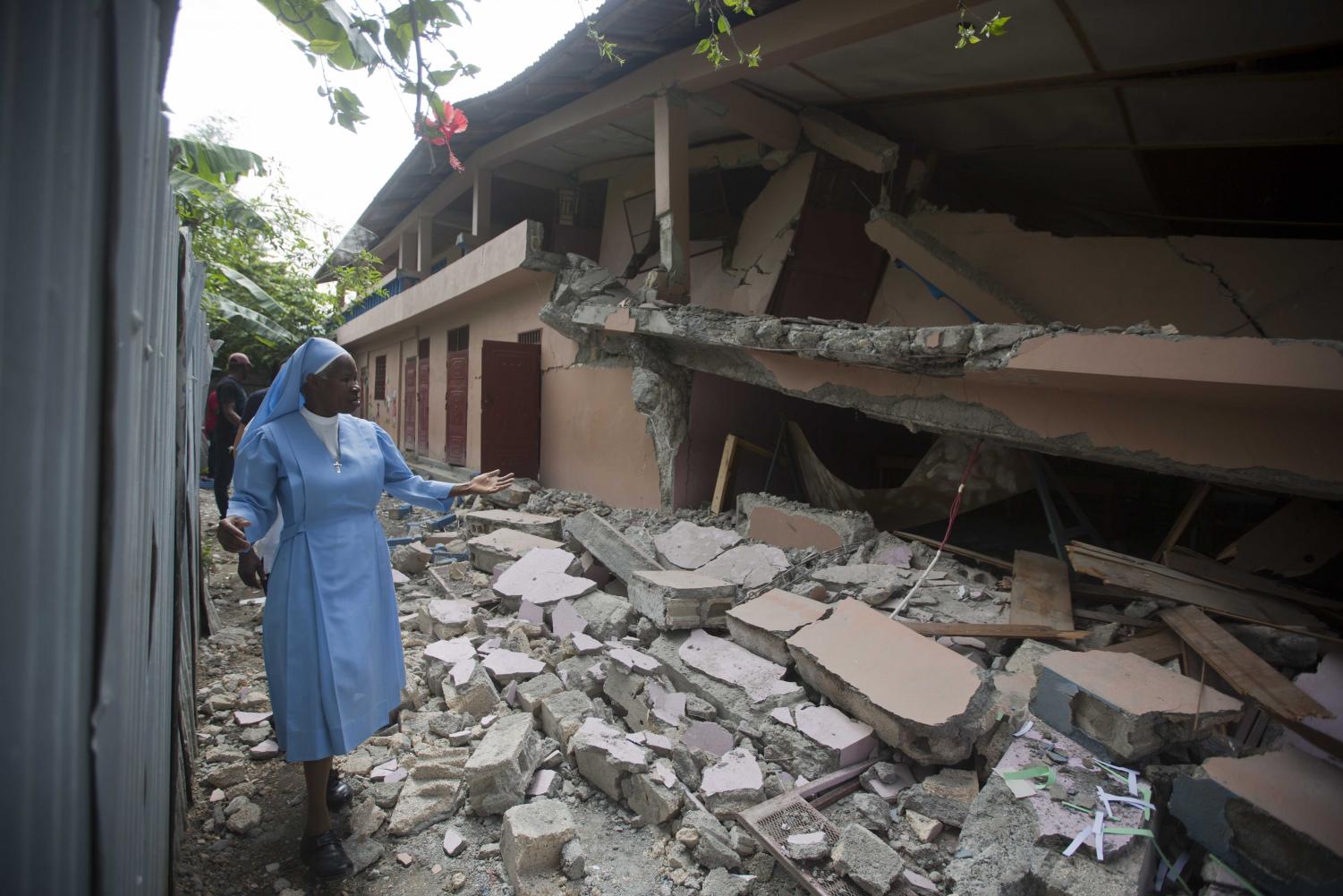 Sr Maryse Alsaint walks alongside a school damaged by a magnitude 5.9 earthquake the night before, in Gros Morne, Haiti, Sunday, Oct. 7, 2018. Emergency teams worked to provide relief in Haiti on Sunday after the quake killed at least 11 people and left dozens injured.