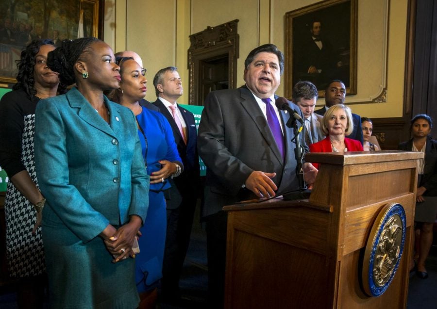 FILE-In this April 9, 2019 file photo, Illinois Governor J.B. Pritzker is flanked by members of the Illinois House and the Illinois Senate as he answers questions after announcing the SJRCA1 Amendment 1, a constitutional amendment to change the states flat income tax to a progressive rate structure, during a news conference in the governors office at the Illinois State Capitol in Springfield, Ill.