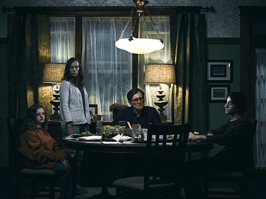 The Graham family — Charlie (Milly Shapiro), Annie (Toni Collette), Steve (Gabriel Byrne) and Peter (Alex Wolff) — sit around the table in “Hereditary.”