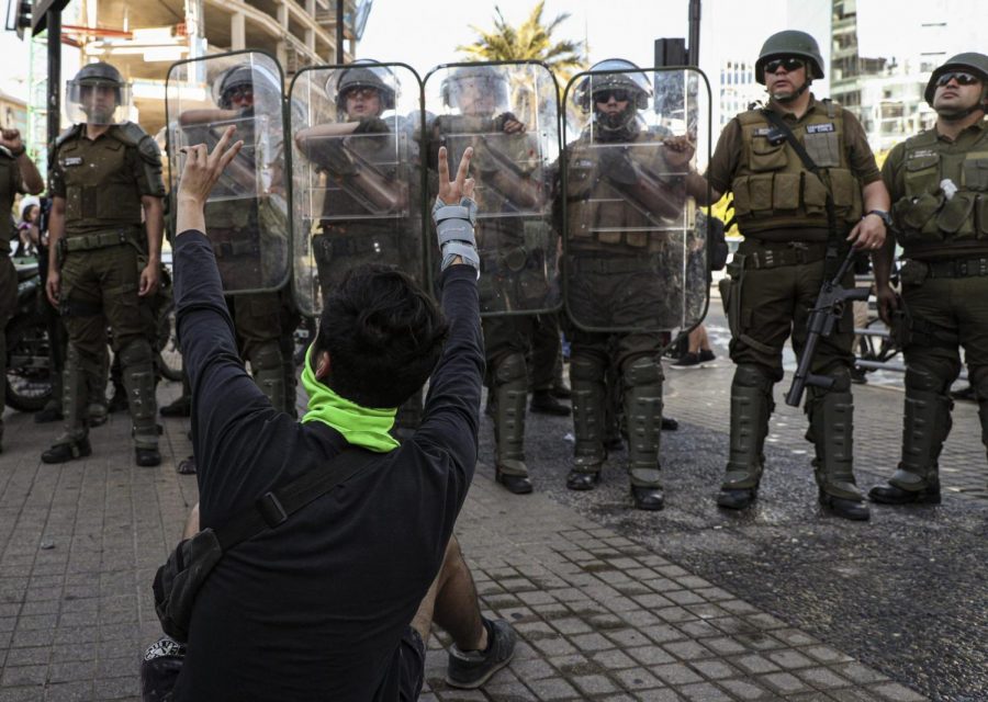 An anti-government protester flashes victory signs at a cordon of Chilean police during in Santiago, Chile, Thursday, Nov. 7, 2019. Twenty people have so far died amid nationwide protests.
