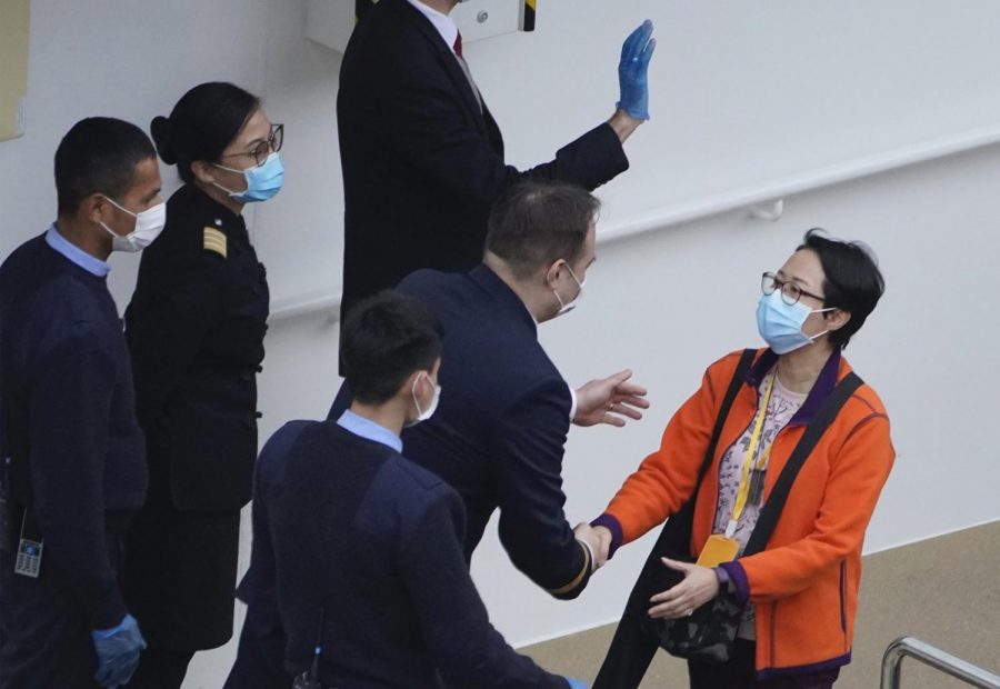 A passenger from the cruise ship World Dream docked at Kai Tak cruise terminal shakes hands with staff as she disembarks the ship after be quarantined for the coronavirus in Hong Kong, Sunday, Feb. 9, 2020. Several passengers from mainland China on a previous World Dream cruise were found to have the new coronavirus on returning home.