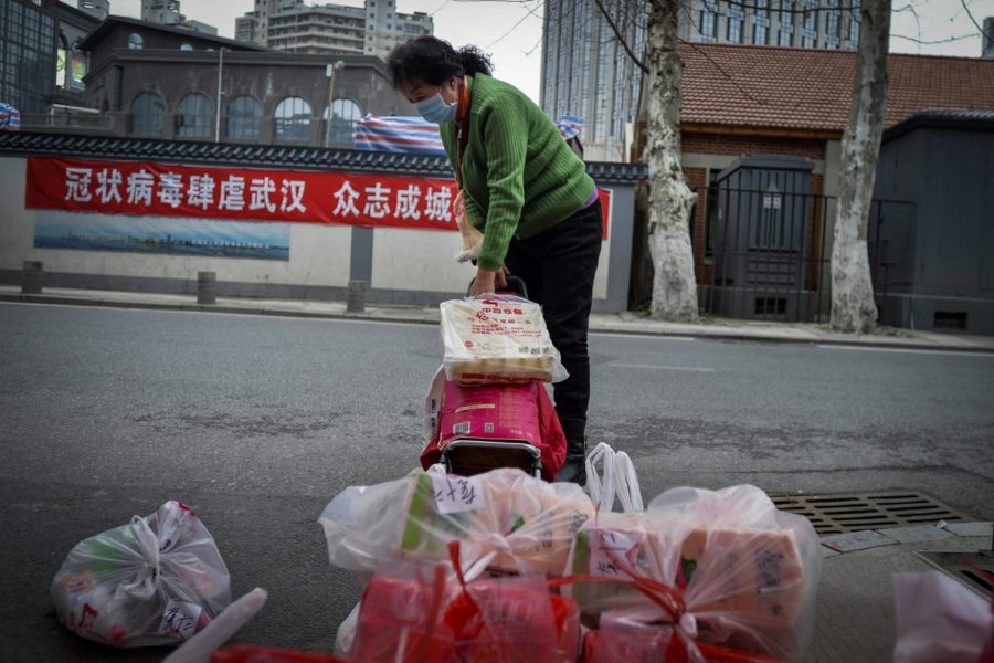 In this Saturday, Feb. 22, 2020, photo, a woman using a trolley bag to collect foods distributed by volunteers outside her home in Wuhan in central China’s Hubei province.