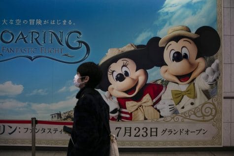 A man wearing a mask walks past an advertisement for the Tokyo Disney Resort at a train station in Urayasu, near Tokyo, Friday, Feb. 28, 2020. The amusement park will be closed from Feb. 29 until March 15 in an effort to prevent the spread of COVID-19.