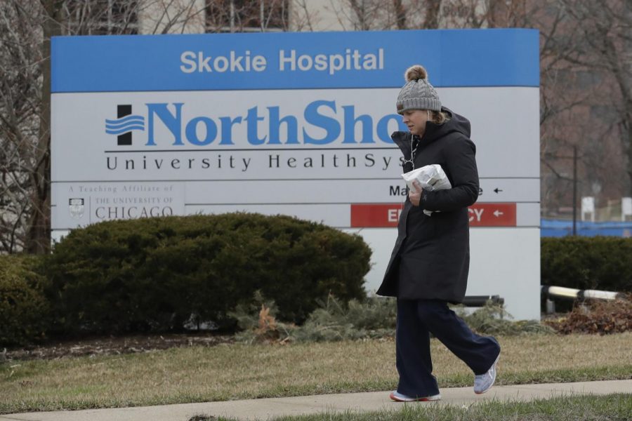 A woman walks on the sidewalk in front of NorthShore Skokie Hospital sign in Skokie, Ill., Friday, March 27, 2020. Gov. J.B. Pritzker issued a stay-at-home order for the entire state, which went into effect on March 21, 2020 and lasts through at least April 7.