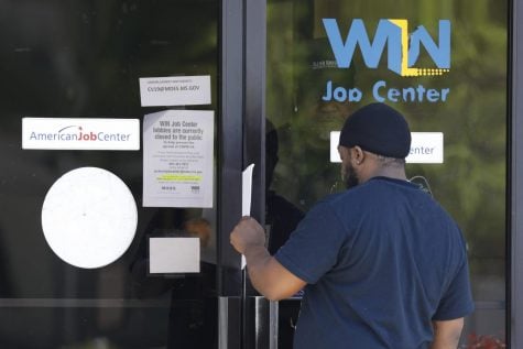 Tyrone Keoton Jr., is handed an unemployment benefit application form by a security guard behind the glass doors of this state WIN Job Center in north Jackson, Miss., Thursday, April 2, 2020. The job centers lobbies are closed statewide to prevent the spread of COVID-19. The agency encourages residents to apply for their benefits on line, however, the system has been stressed by the large numbers of applicants. The local job centers are making paper unemployment applications available and applicants are filling them out and pushing them back through the mail slots or doors as well as they can.