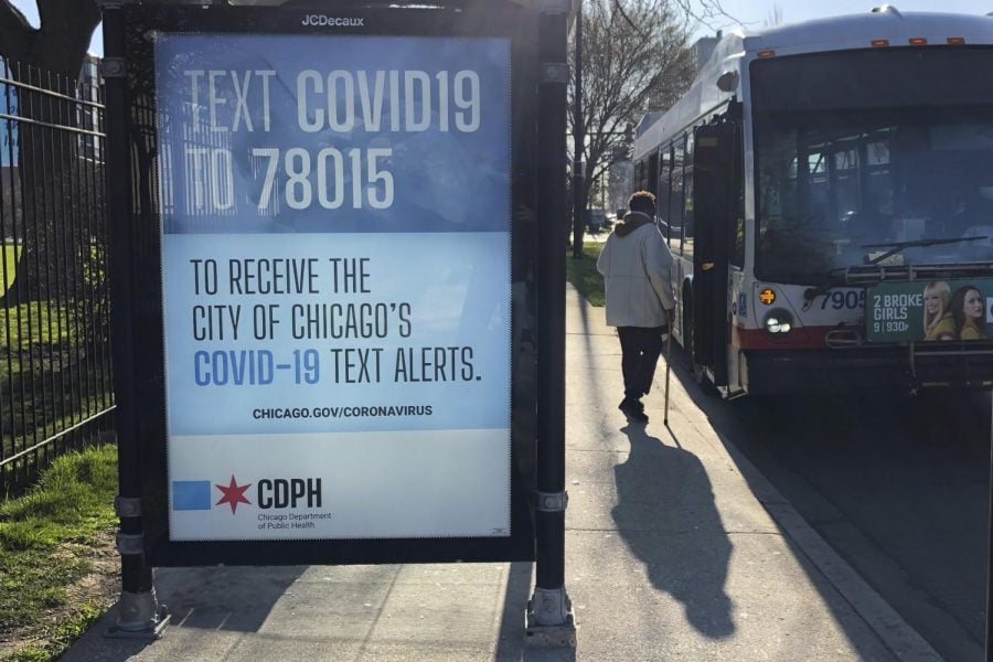 A+lone+woman+boards+a+Chicago+Transit+Authority+bus+in+the+Bronzeville+neighborhood+of+Chicago%2C+Monday%2C+April+20%2C+2020%2C+as+a+public+service+billboard+reminds+people+of+the+continuing+fight+against+COVID-19.