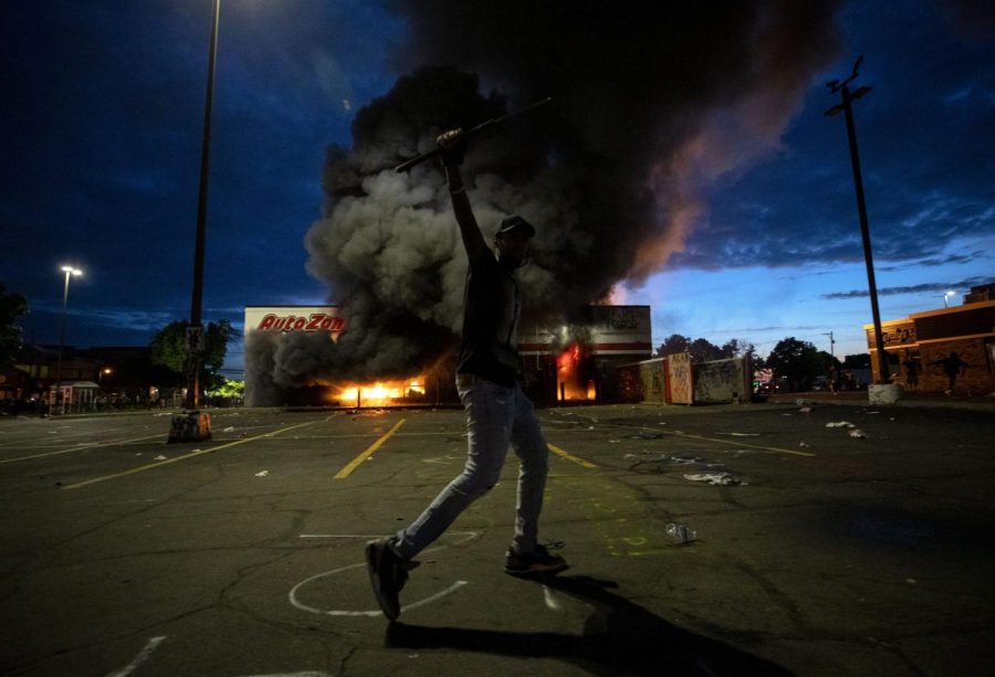A man poses for a photo in the parking lot of an AutoZone store in flames, while protesters hold a rally for George Floyd in Minneapolis on Wednesday, May 27, 2020. Violent protests over the death of the black man in police custody broke out in Minneapolis for a second straight night Wednesday, with protesters in a standoff with officers outside a police precinct and looting of nearby stores.