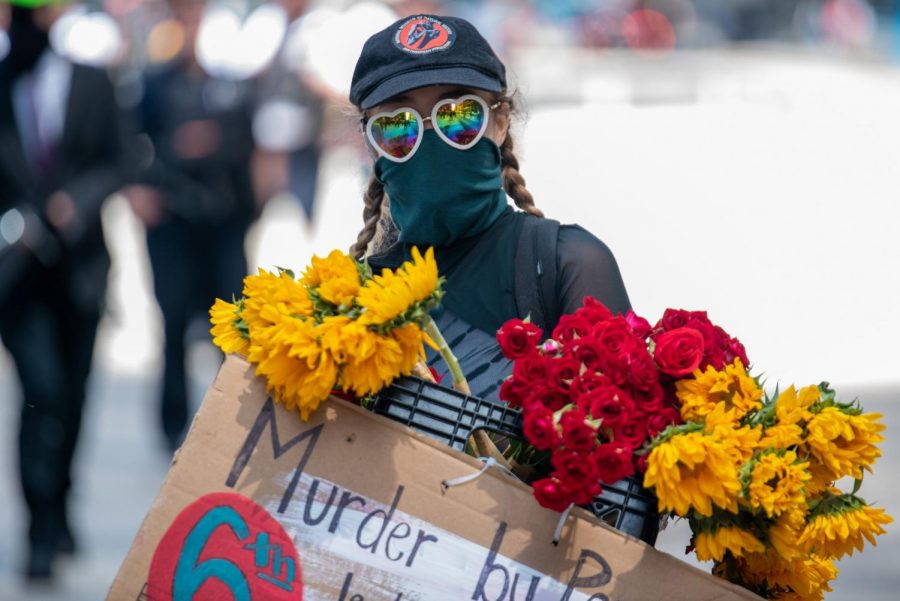 A masked protester holds a sign and flowers.
