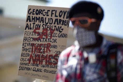 Ismael Kamara stand in front of a poster with names from people died after police violence the demonstrators say, as he attends a rally to commemorate George Floyd and against racism and police violence in front of the Brandenburg Gate in Berlin, Germany, Monday, June 1, 2020. Floyd died after being restrained by Minneapolis police officers on Memorial Day May 25.