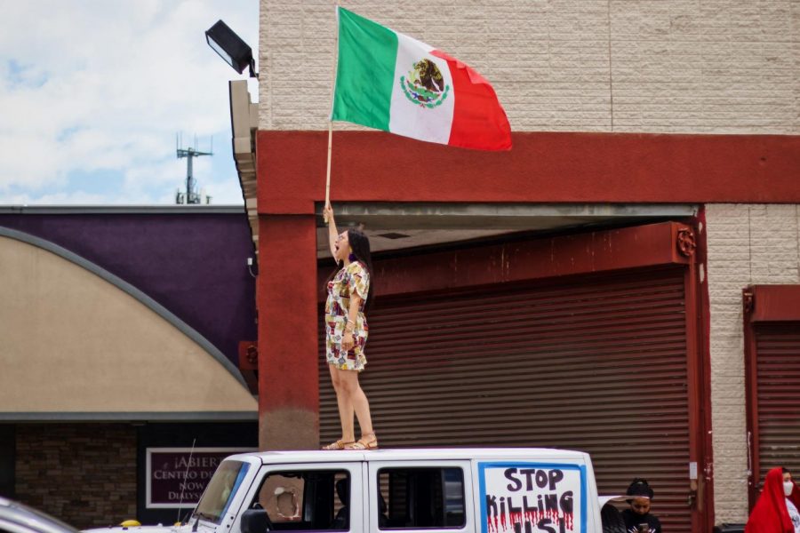 Una mujer se pone de pie sobre un vehículo ondeando la bandera mexicana.
A woman stands on top of a vehicle waving the Mexican flag. 