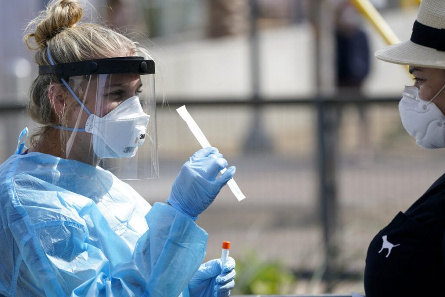 FILE - In this Aug. 13, 2020, file photo, nurse practitioner Debbi Hinderliter, left, collects a sample from a woman at a coronavirus testing site near the nations busiest pedestrian border crossing in San Diego. The credibility of two top public health agencies is on the line after controversial decisions that outside experts say suggest political pressure from the Trump administration. The Centers for Disease Control and Prevention triggered a backlash from the medical community by rewriting its guidelines to recommend less testing. (AP Photo/Gregory Bull, File)