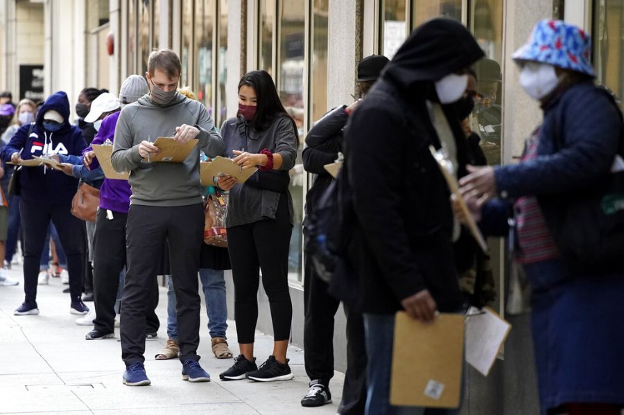People wait line to early vote as they fill out voter registration cards outside the Loop Super Site in downtown Chicago, Sunday, Oct. 11, 2020. It is the only location allowing early voting in the city right now, but early voting will expand to locations in all 50 wards on Oct. 14. (AP Photo/Nam Y. Huh)