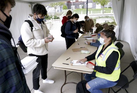 FILE-Elizabeth Quirmbach, right, registers Ayuka Sinanoglu, center, a Sophomore at the UW on Wednesday, Oct. 19, 2020  outside of the UW Memorial Union in Madison, Wis.  A small but steady stream of masked UW-Madison students stopped by voter registration tables outside the unions last week to perform their civic duty. Madison City Clerk’s office employees helped them through the paperwork, sanitized their used pens and talked among themselves as they waited for the next students to filter into the fairly empty tents.(Steve Apps/Wisconsin State Journal via AP)