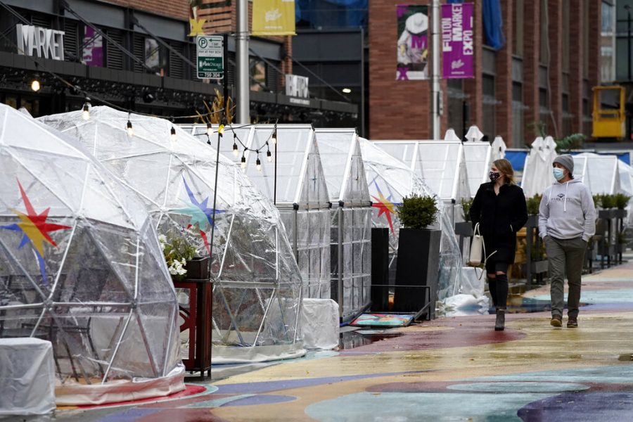 People walk by outdoor plastic dining bubbles on Fulton Market in Chicago, Sunday, Oct. 18, 2020. Colder temperatures are providing a new challenge for restaurants during the coronavirus pandemic, but there's a solution being developed in Fulton Market. (AP Photo/Nam Y. Huh)