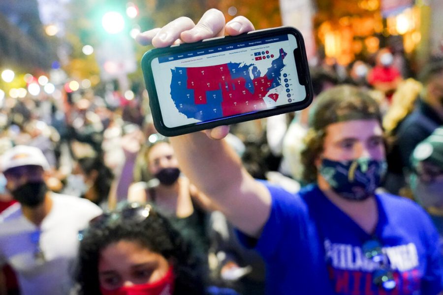 A supporter of President-elect Joe Biden holds up his mobile phone to display the electoral college map outside the Philadelphia Convention Center after the 2020 Presidential Election is called, Saturday, Nov. 7, 2020, in Philadelphia. (AP Photo/John Minchillo)