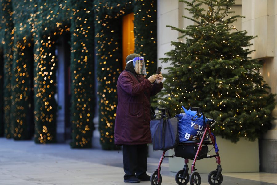 A woman photographs Christmas decorations on Oxford Street during a second lockdown in London, Thursday, Nov. 19, 2020. Businesses that have been forced to shut are hoping they will be able to reopen to salvage something of the crucial holiday shopping season. The government has been reluctant to say what restrictions will be in place for any particular area when the lockdown ends and says it's still too early to see how the lockdown has worked. (AP Photo/Kirsty Wigglesworth)