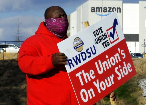 FILE - In this Tuesday, Feb. 9, 2021, file photo, Michael Foster of the Retail, Wholesale and Department Store Union holds a sign outside an Amazon facility where labor is trying to organize workers in Bessemer, Ala. Nearly 6,000 Amazon warehouse workers in Bessemer, Alabama, have voted on whether or not to form a union. But the process to tally all the ballots and determine an outcome will continue for a second week, according to the National Labor Relations Board, a government agency that’s conducting the election.(AP Photo/Jay Reeves, File)