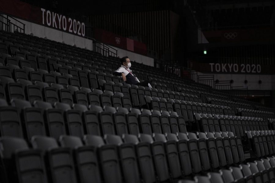 A man, wearing a protective face mask, sits inside an empty Ariake Arena, just before the start of a womens volleyball preliminary round pool A match between Japan and South Korea, at the 2020 Summer Olympics, Saturday, July 31, 2021, in Tokyo, Japan. (AP Photo/Manu Fernandez)
