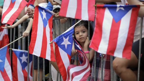 Una niña observa cómo la gente levanta banderas puertorriqueñas en el desfile del Día Nacional de Puerto Rico.