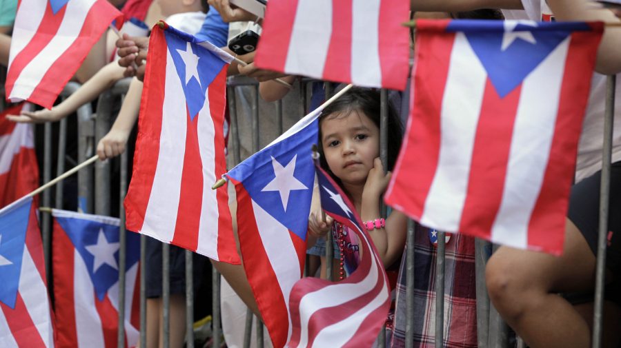 Una+ni%C3%B1a+observa+c%C3%B3mo+la+gente+levanta+banderas+puertorrique%C3%B1as+en+el+desfile+del+D%C3%ADa+Nacional+de+Puerto+Rico.