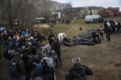 Journalists report as forensic workers line up the corpses of civilians collected from a mass grave in Kyiv, Ukraine, Friday, April 8, 2022.