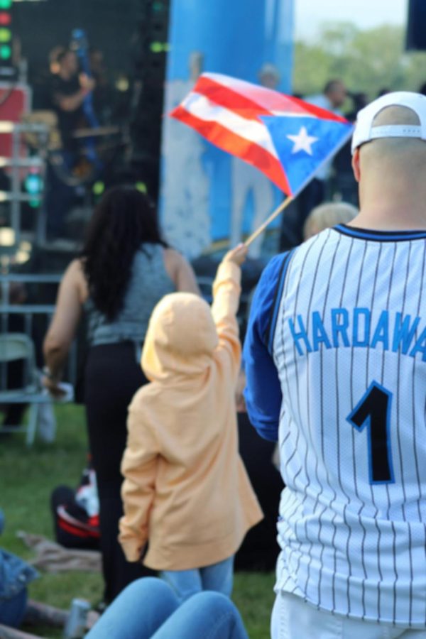 Un niño ondea su bandera puertorriqueña con orgullo mientras observa a los artistas cerca del escenario de las Fiestas Patronales Puertorriqueñas.