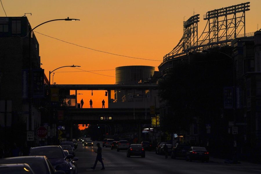 Commuters waiting for Chicagos L train are silhouetted against the sunset-colored sky at Addison Station next to Wrigley Field baseball park, right, Monday, Sept. 19, 2022, in Chicago.