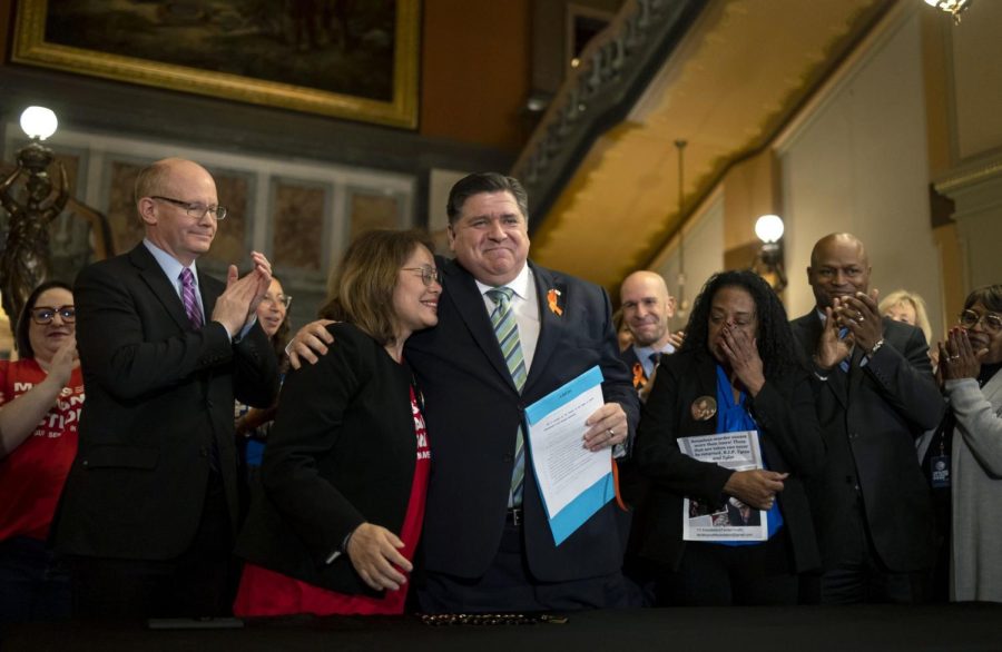 Gov. J.B. Pritzker hugs gun control advocate Maria Pike after he signed comprehensive legislation to ban military-style firearms on Tuesday. Pike lost her son, Ricky, to gun violence. Advocate Delphine Cherry, third from right, who lost her children to gun violence, wipes away tears.