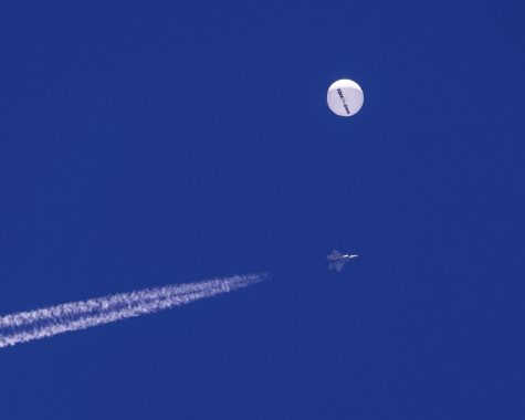 A large balloon drifts above the Atlantic Ocean, just off the coast of South Carolina, with a fighter jet and its contrail seen below it.