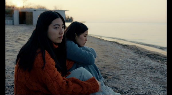 Jin Park and Joyce Ha sit on a beach in a still from the film Waiting for the Light to Change.