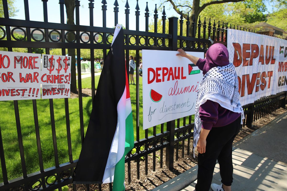 An organizer hangs a sign outside DePaul’s quad, on April 30, reading “DePaul Alumni for Divestment.”  
