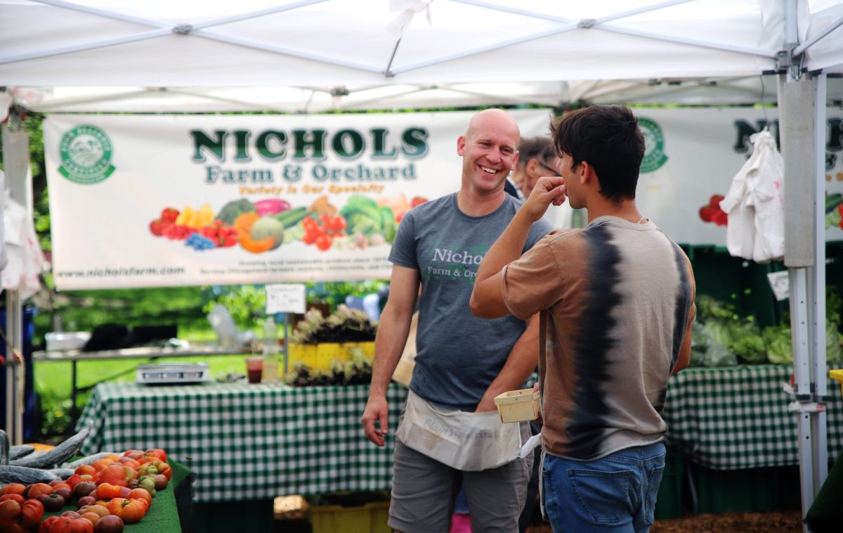Nichols Farm & Orchard employees Steve Freeman, left, and Aiden Nichols chat at their stand in the Lincoln Park Green City Market on Wednesday, May 8, 2024. Freeman has enjoyed working at Nichols Farm & Orchard for 20 years and Nichols has been involved with the farm all his life. Both enjoy the atmosphere and community of the market.