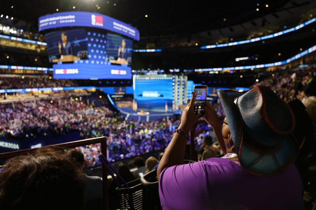 A spectator takes a photo of the jumbotron during night one of the DNC, on Aug. 19, 2024, at the United Center in Chicago. 