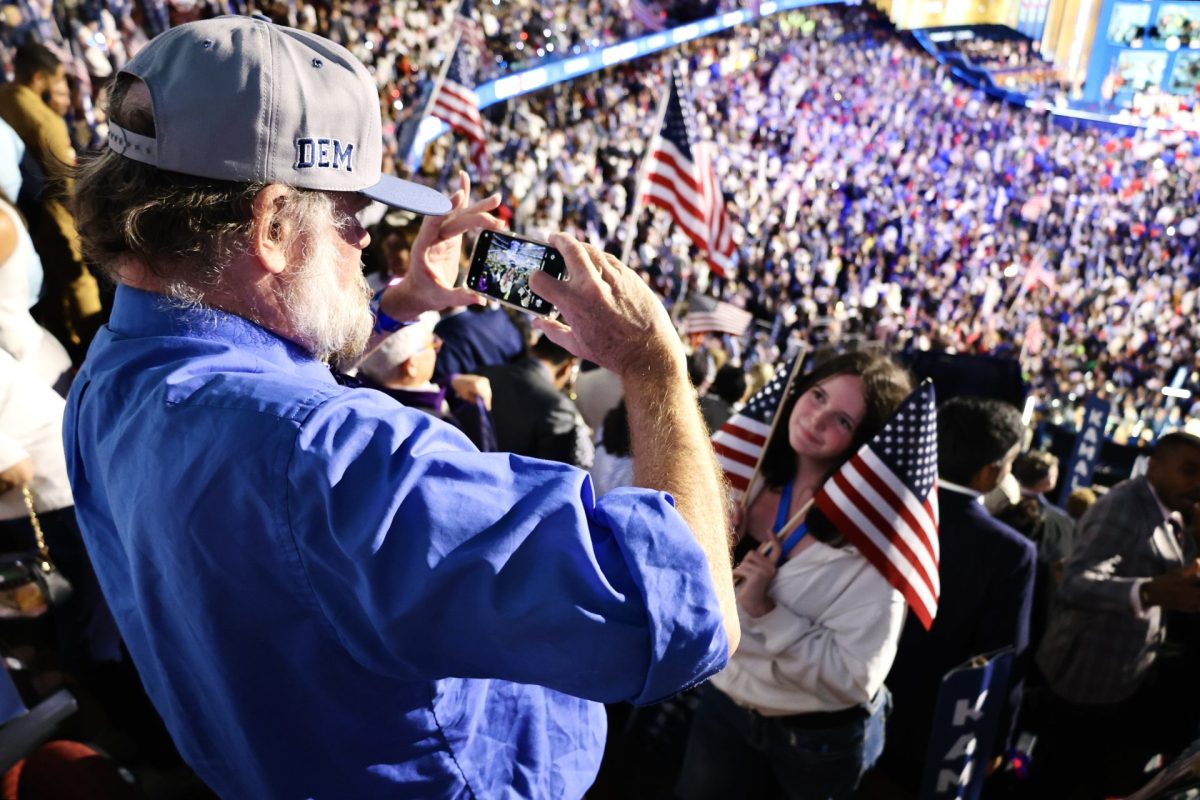 A father takes a photo of his daughter who poses with two American flags during the last day of the Democratic National Convention, on Aug. 22, 2024.