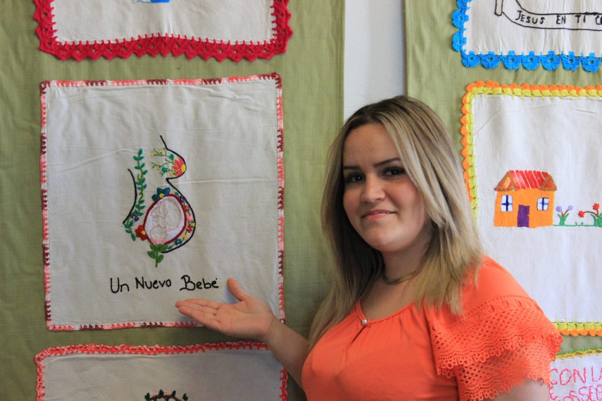 Wendy Lopez Aguilar poses beside one of her hand-embroidered mantas, or decorative serving napkins, on display at Casa de Cultura in the Bordando Esperanza exhibit in Chicago on Sept. 21, 2024. The exhibit is curated by Artisans Beyond Borders, an organization providing resources to migrants.