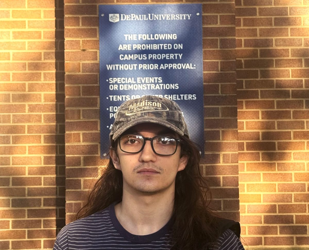 Grey Light stands in front of a sign outlining protest policies on Wednesday, Sept. 25, 2024, at the Lincoln Park campus. Light is a junior and photographer studying at Roosevelt College and has photographed protesting students, believing they are not a threat.