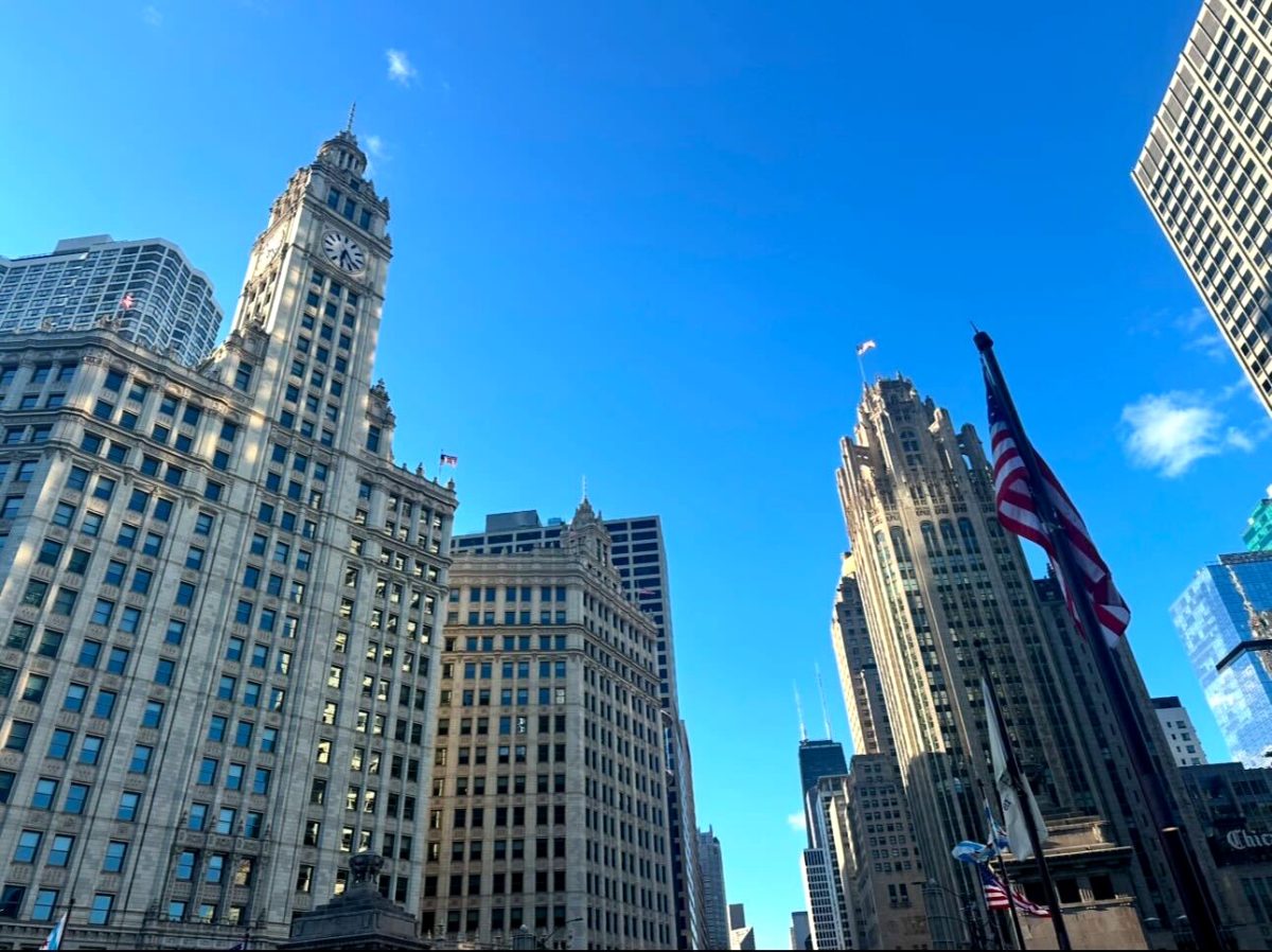 Chicago’s skyline features the Wrigley Building and the Tribune Tower beneath a clear blue sky as an American flag stands in the foreground on July 29, 2024.