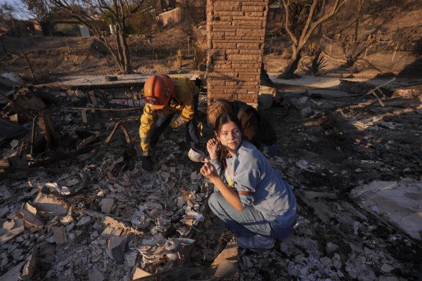 Ella Venne, front, holds a cup she found in the remains of her family's home destroyed by the Eaton Fire as she searches with Glendale Fire Department captain Chris Jernegan, left, and his wife Alison in Altadena, Calif., Saturday, Jan. 11, 2025