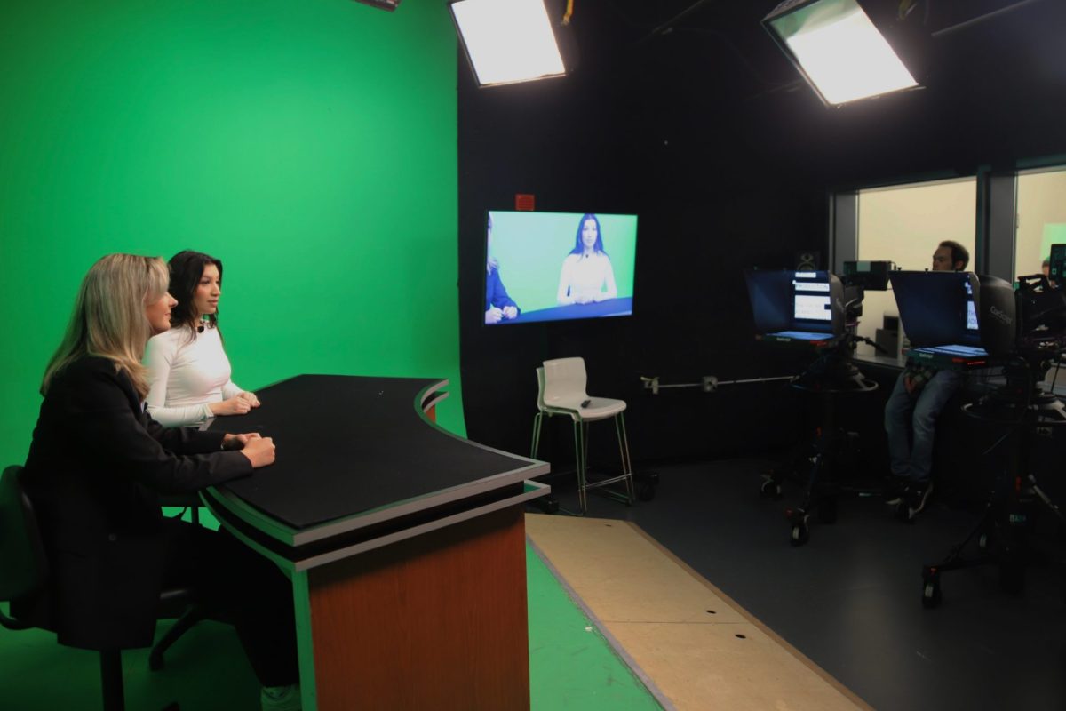 Riley Moulton, left, and Tori Trevino, right, sit at an anchor desk on Wednesday, April 16, 2025, during the first in-person taping of 'Good Day DePaul' since the COVID-19 pandemic. The students, both juniors, hope to start their career in television news broadcasting.